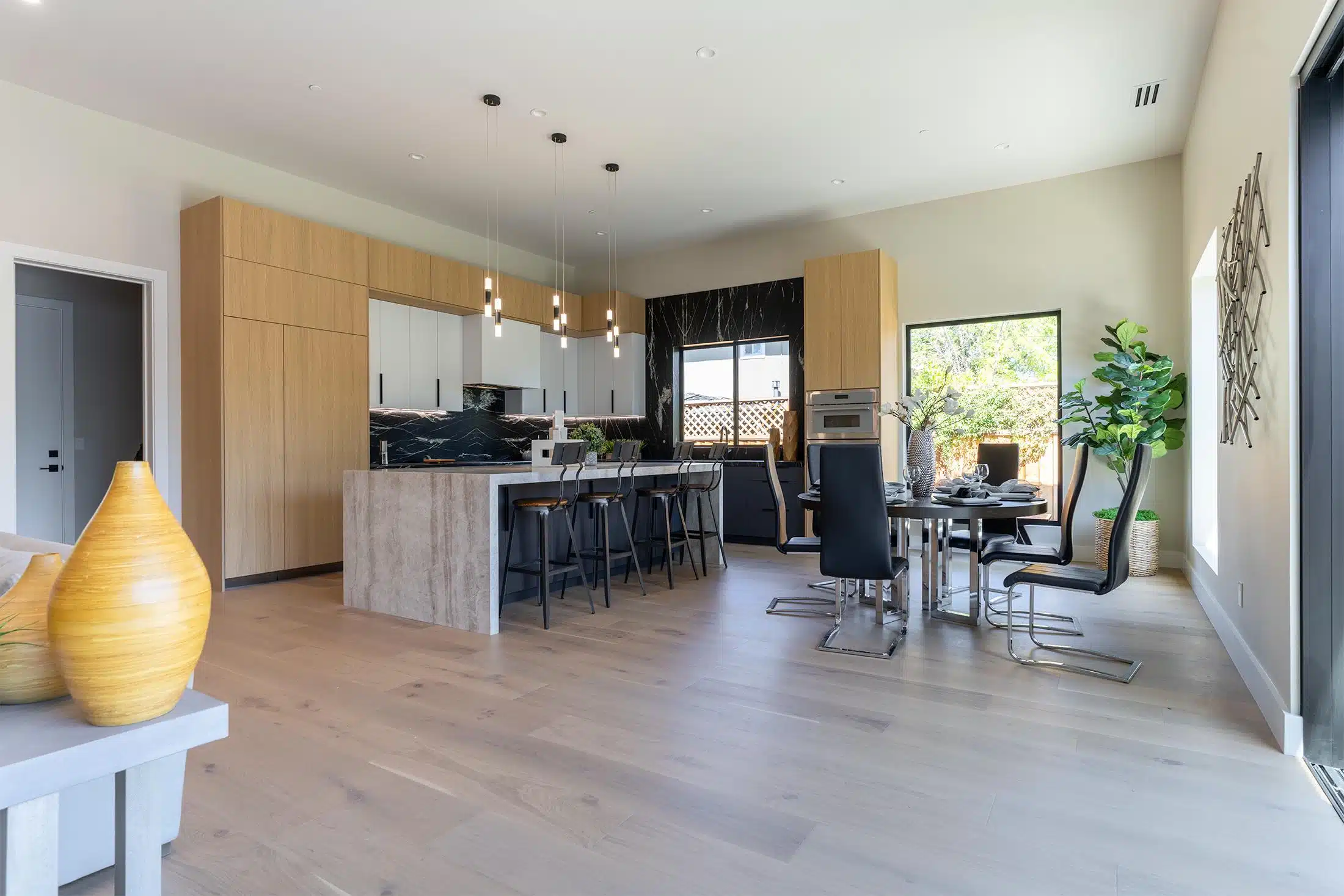 Open-plan kitchen remodel with oak and white cabinets, a black marble feature wall and a travertine waterfall island
